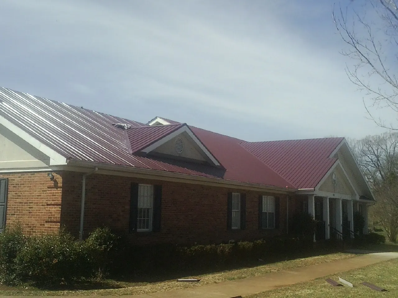 Red metal roof with gabled entries on a long brick building, from a Hail Damage Roof Repair job in Hanscom Afb