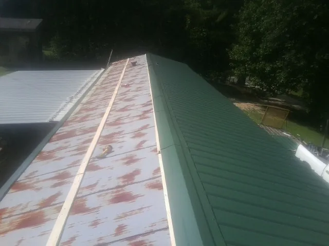 Old rusted panels beside newly installed green metal roofing — Wind Damage Roof Repair by Roofing Brothers in Hanscom Afb