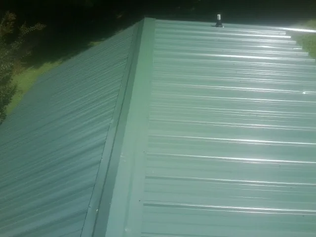 New green metal panels meeting at the ridge of a roof — Flat Roof Repair work by our crew in Hanscom Afb